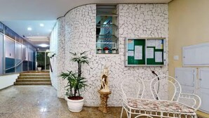 A hallway with a white textured wall, a statue, a potted plant, and a white metal chair. - 360 Aterro do Flamengo By SUHCasa (Rio de Janeiro)