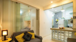 A modern living room with a sofa, a small table, and a glass partition leading to a kitchen area. - 360 Aterro do Flamengo By SUHCasa (Rio de Janeiro)