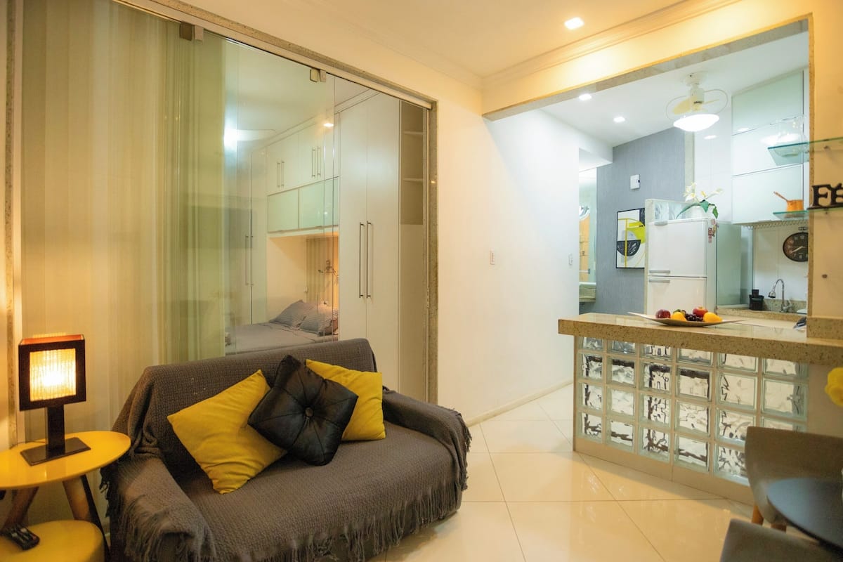 Un salón moderno con un sofá, una mesita y un separador de vidrio que da a una zona de cocina.