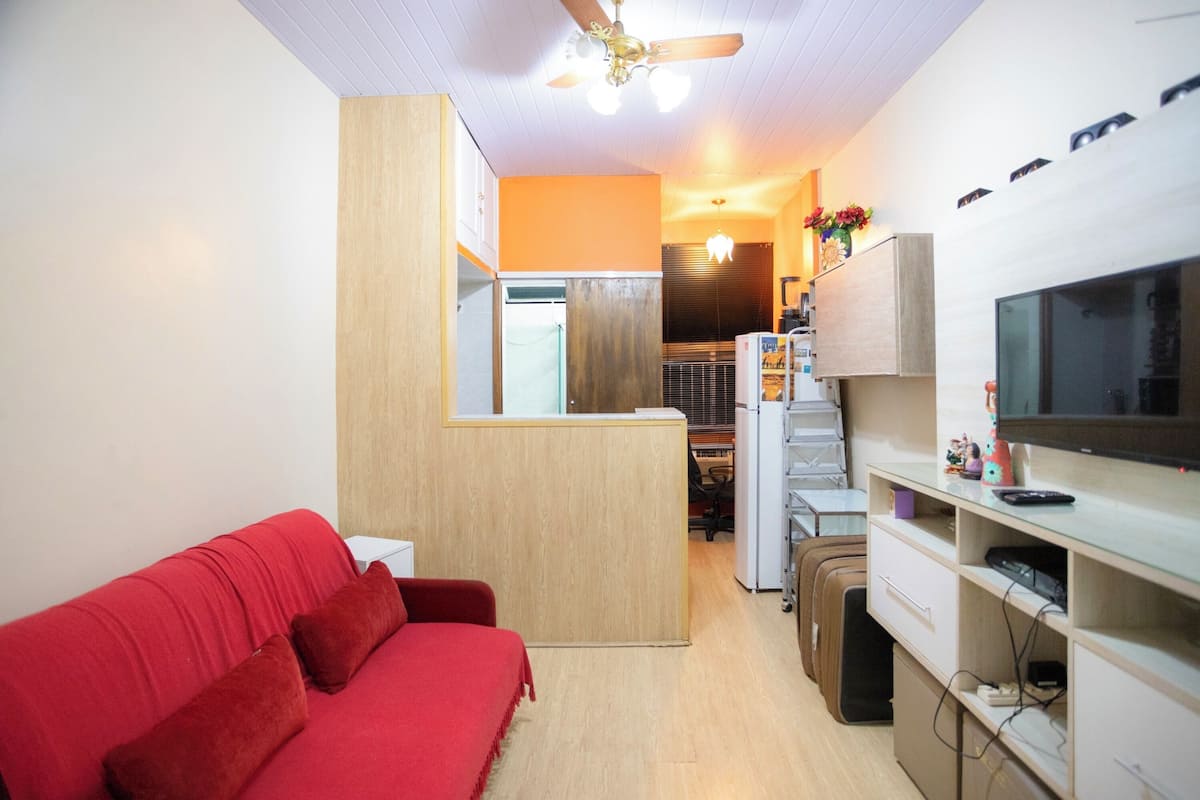 Un espacio habitable compacto con un sofá rojo, kitchenette, televisor y ventilador de techo.
