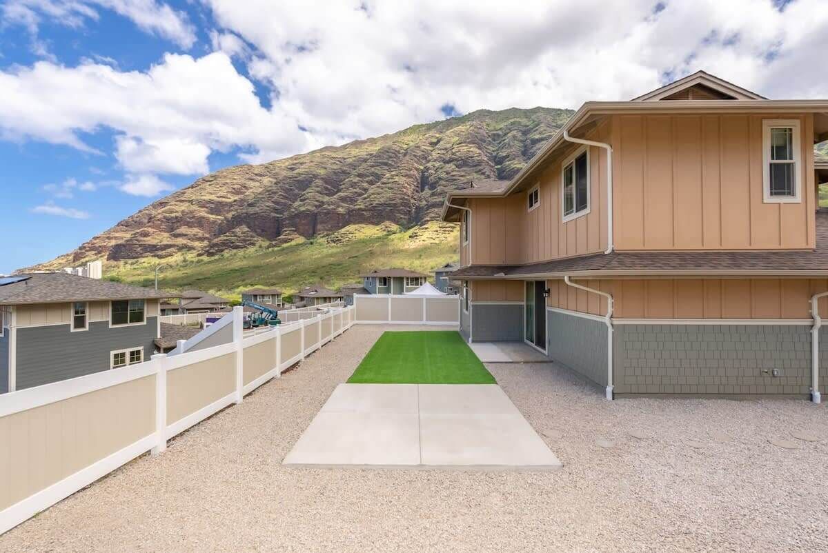 A residential area with a house featuring a front yard with a green lawn and a gravel driveway.