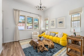 Una sala de estar con un sofá amarillo, una mesa de centro de madera y una araña.