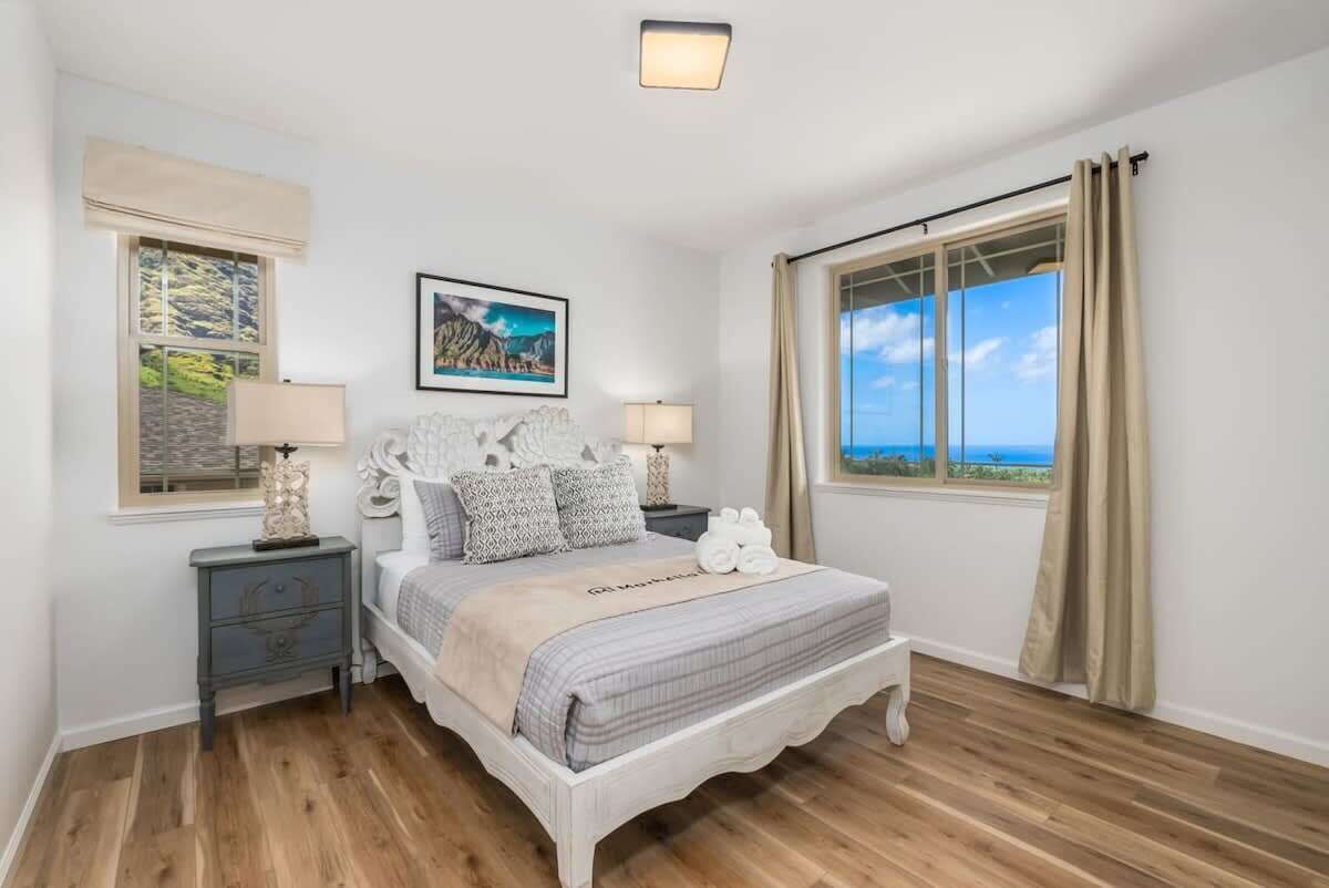 A bedroom with a large bed, two bedside tables, a window with curtains, and a painting on the wall.