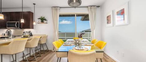 A modern kitchen with dark cabinets, a microwave, and a dining area with a glass table and yellow chairs.