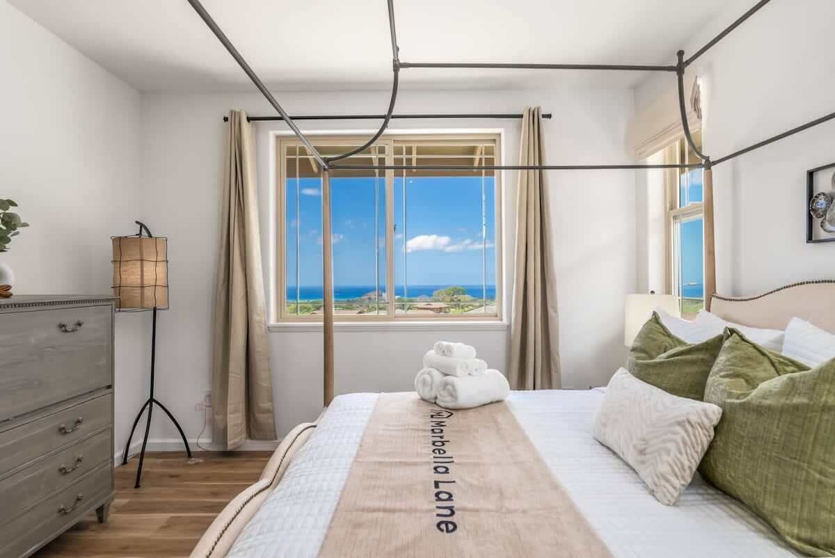 A bedroom with a bed, a view of the sea, a lamp, and a dresser.
