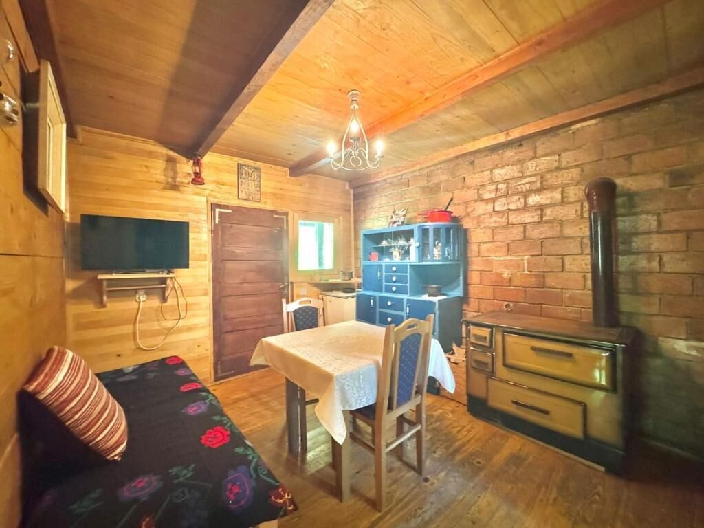 A cozy cabin interior with a wooden dining table, a sofa with a floral cover, a brick wall, and a fireplace.