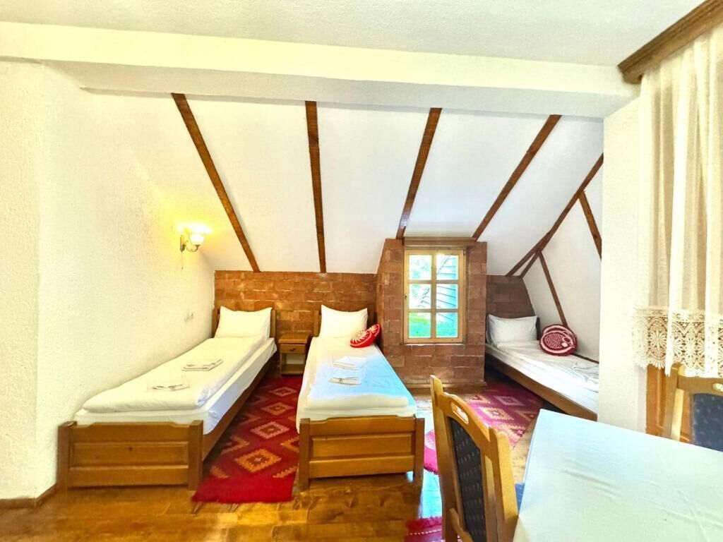 Un dormitorio acogedor y pequeño en el ático, con dos camas individuales, techo de madera y un ventanal.