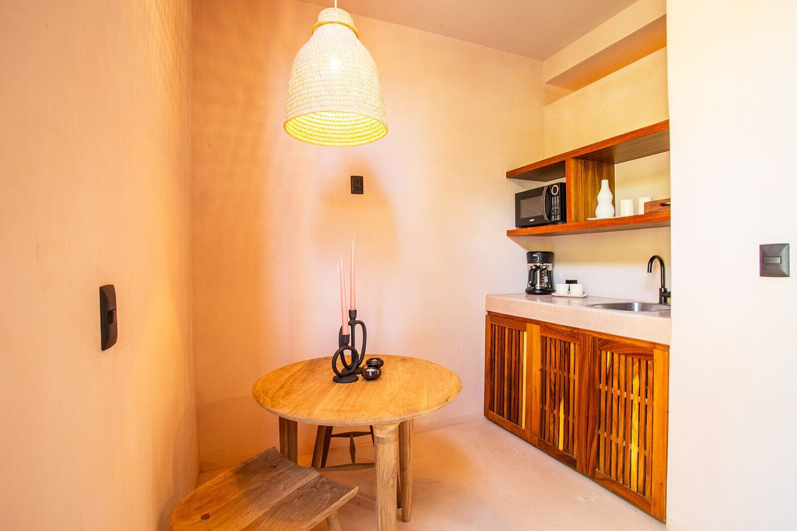 Cocina compacta con una mesa redonda de madera, una lámpara colgante y un microondas en un estante.