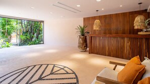A modern reception area with a wooden reception desk, a large potted plant, and a view of greenery outside. - Marakame San Pancho (San Francisco)