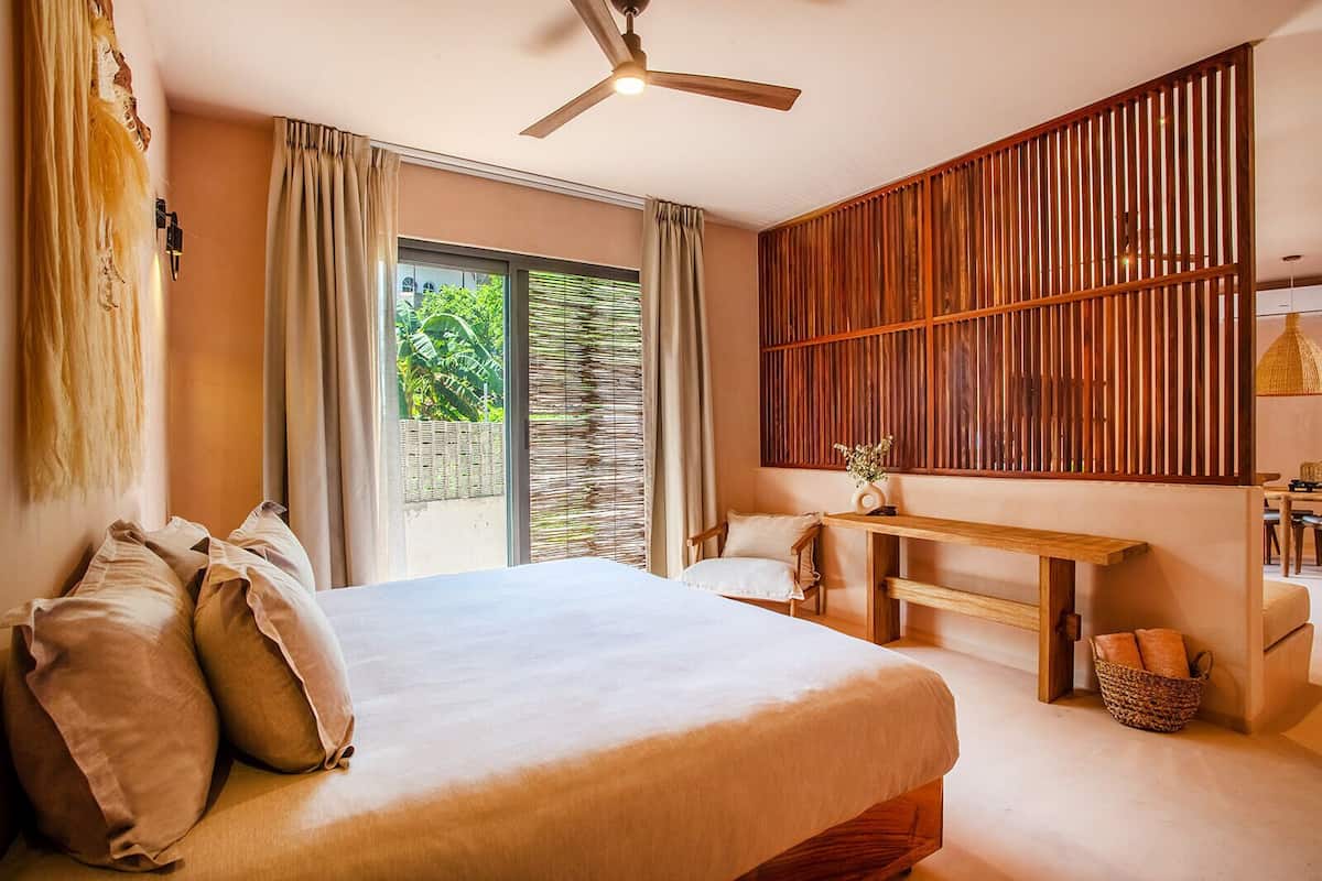 A bedroom with a bed, a desk, and a view of greenery outside.