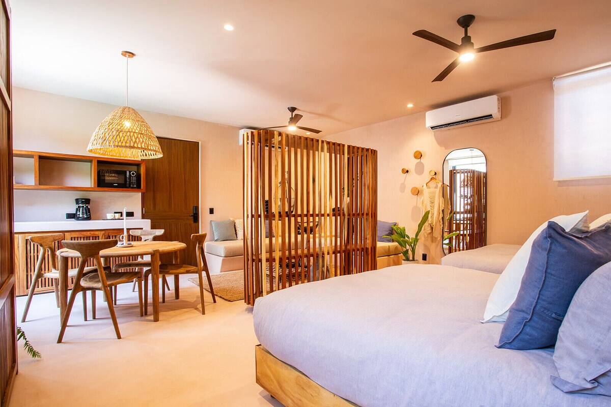 A modern bedroom with a large bed, a dining area with a table and chairs, a kitchen area with a microwave, and a ceiling fan.