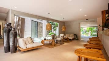 A spacious living area with a sofa, chairs, and a coffee table. There are large windows and a view of greenery outside.