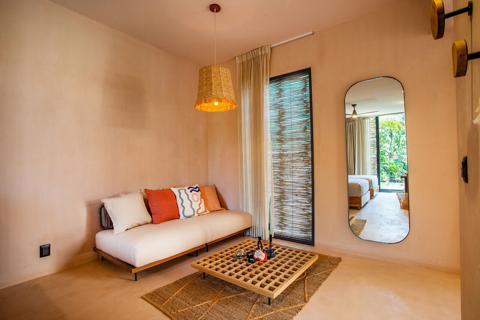 A modern bedroom with a sofa, a wooden coffee table, a large mirror, and a view of the outdoors.
