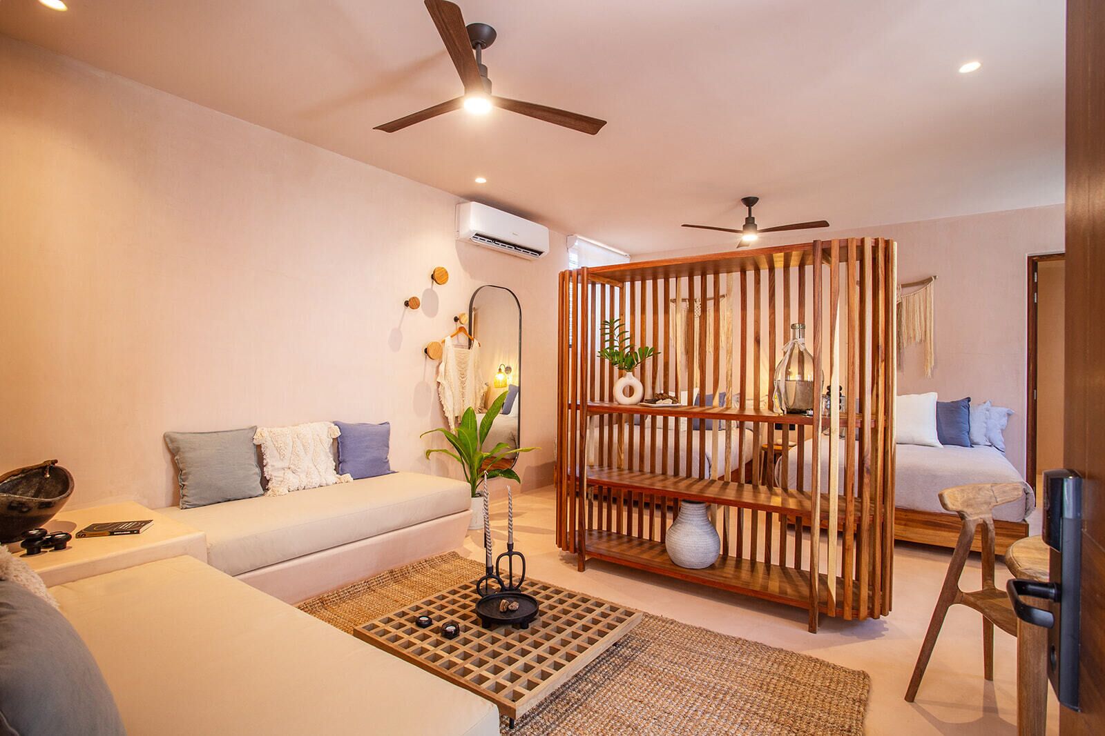Een moderne woonkamer met een witte bank, een houten scheidingswand en een plafondventilator.