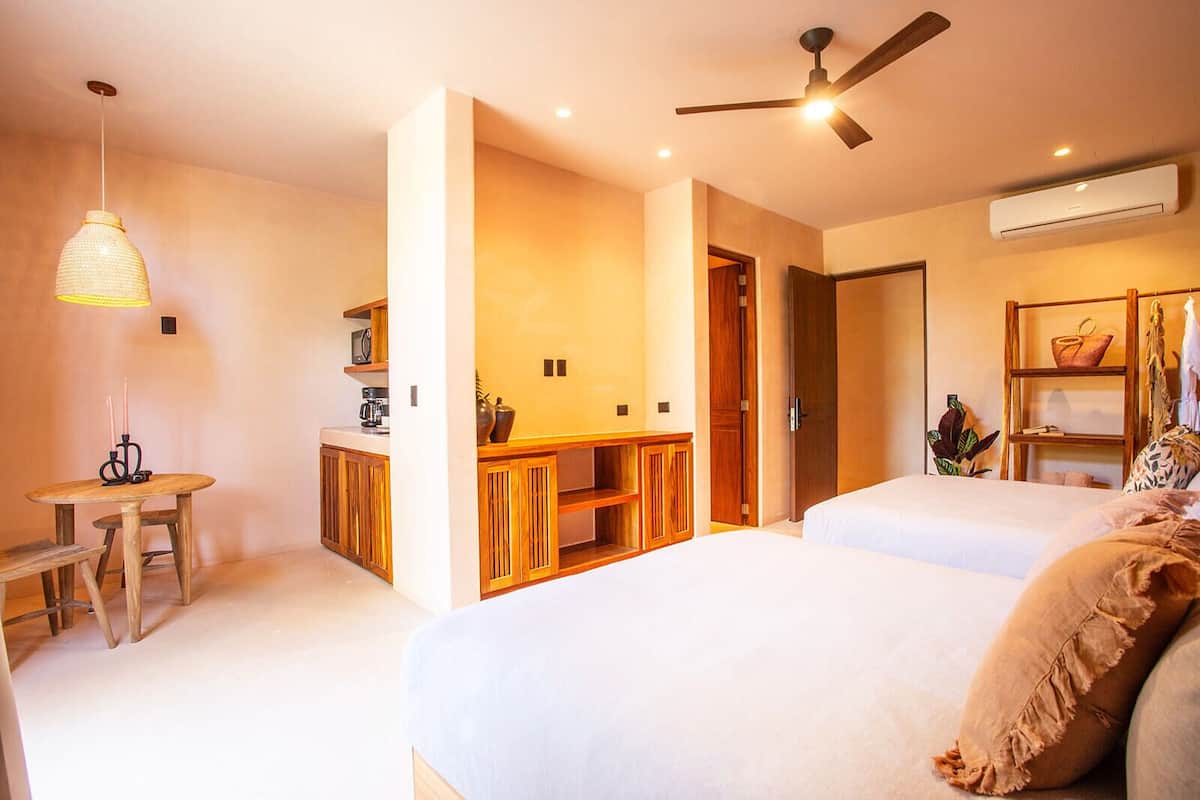 A bedroom with two beds, a desk, and a kitchenette.