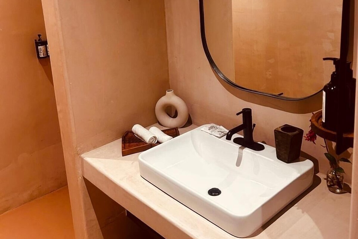 A bathroom with a white sink, a mirror, a towel, and a shower head.