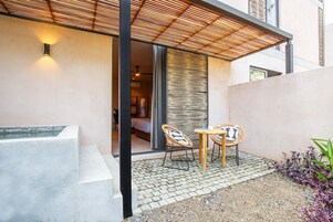 Un patio moderno al aire libre con dos sillas de mimbre, una mesita y un muro decorativo.