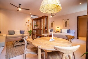 Una sala de estar moderna con una mesa redonda de madera, dos sofás, un ventilador de techo y una lámpara colgante decorativa.
