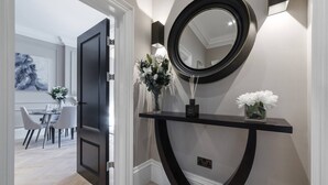 A modern hallway with a black console table, a round mirror, and a vase with white flowers.