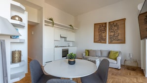 A modern living room with a round white table, grey chairs, a grey sofa, and a white kitchen in the background.