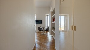 A hallway with a wooden floor, a dining area with a table and chairs, and a TV mounted on the wall.