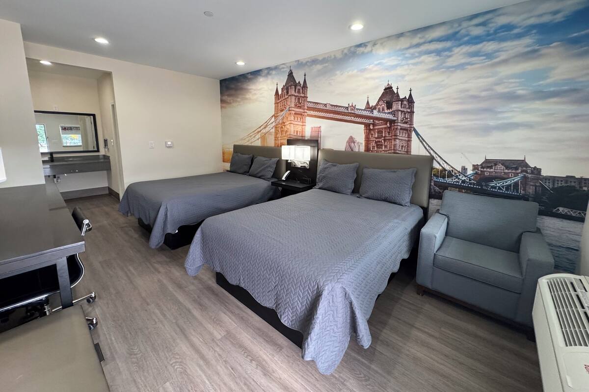 Una habitación de hotel con dos camas, un escritorio, una silla y un gran mural de un puente.