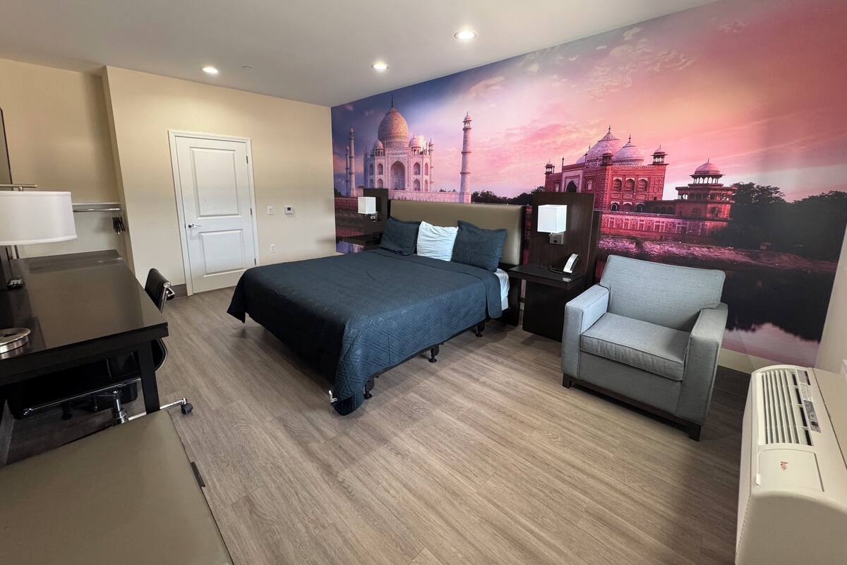 Una habitación de hotel con una cama, un escritorio, una silla y un mural grande de un edificio histórico.