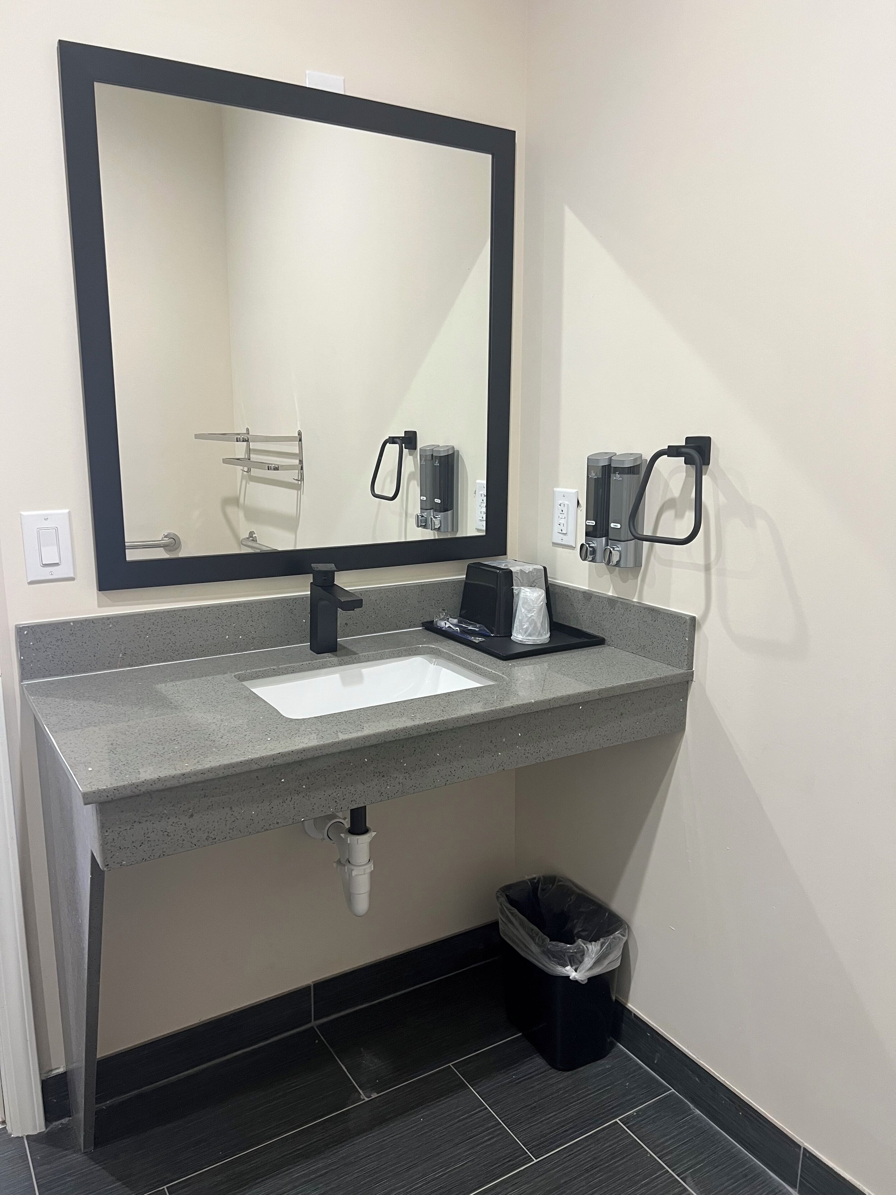 Un baño moderno con un espejo grande, un lavabo y un cubo de basura.