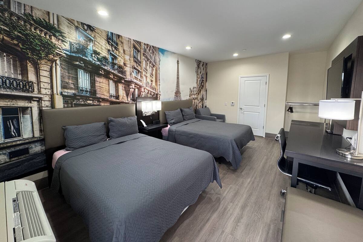 Habitación de hotel con dos camas, un escritorio, una silla, una lámpara de escritorio, un televisor montado en la pared y una puerta.