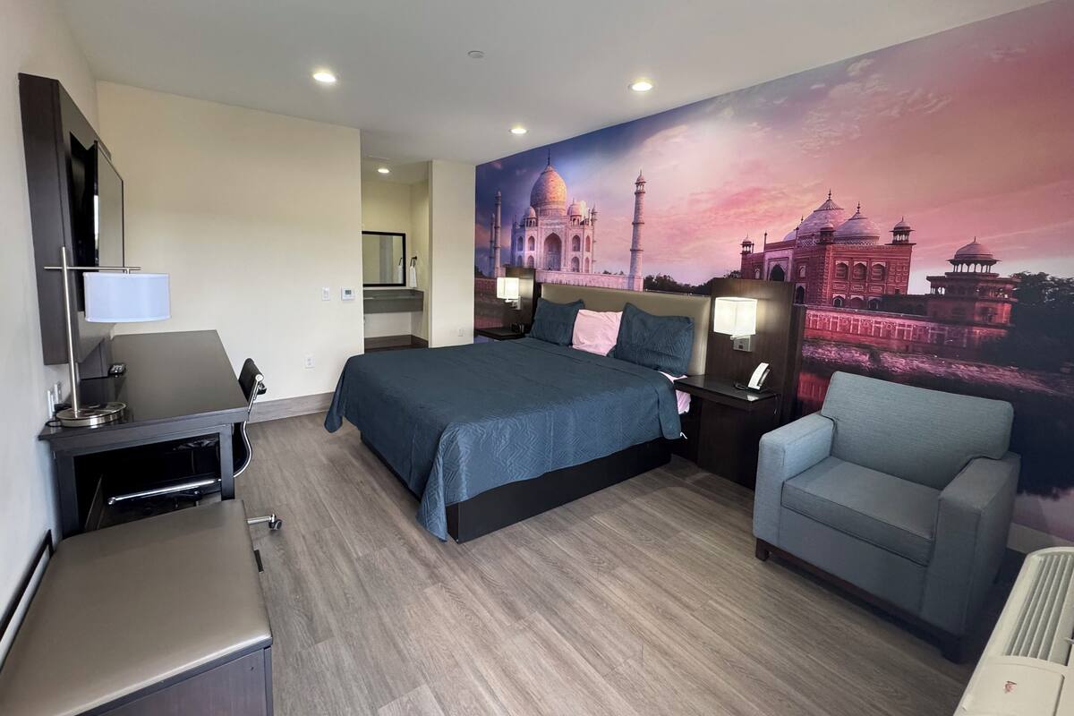 Una habitación de hotel con cama, escritorio, silla y un mural en la pared de un monumento famoso.