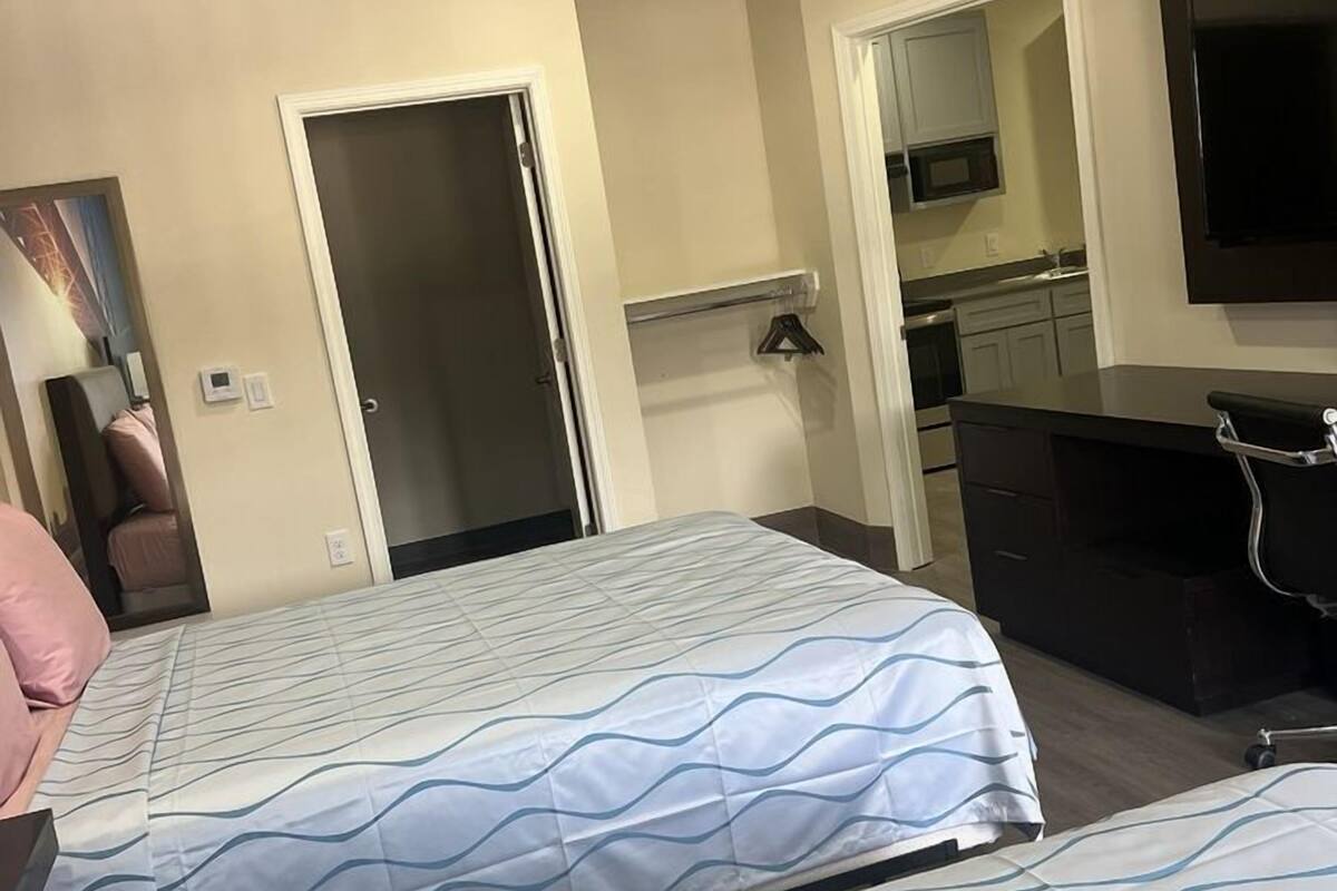 Habitación de hotel con cama, escritorio, silla, televisor y kitchenette.