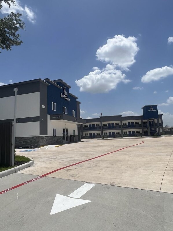 A building with a blue and white facade, a parking lot with marked lanes, and a clear sky with clouds. - Elite Inn & Suites (Houston)