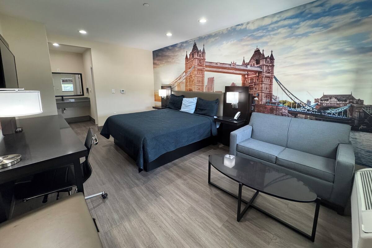 Habitación de hotel con cama, escritorio, silla, sofá y un mural de un puente.
