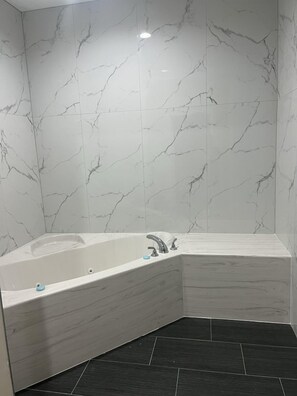A corner bathroom with a freestanding bathtub, white marble walls, and dark floor tiles. - Elite Inn & Suites (Houston)