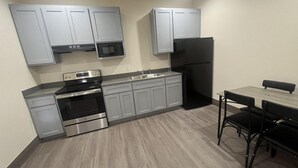 Une cuisine moderne avec des meubles gris, un réfrigérateur noir, des appareils en acier inoxydable et un coin repas comprenant une table en bois et des chaises noires.