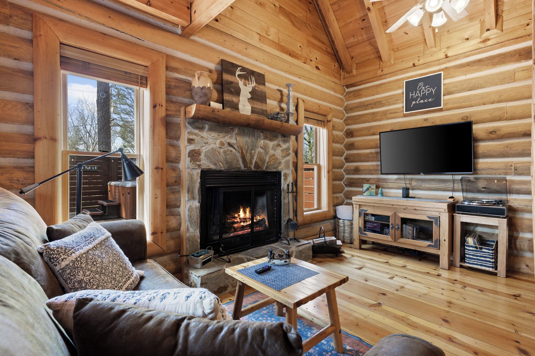 A log cabin interior with a stone fireplace, a television, a sofa, and a wooden entertainment unit.