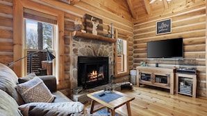 A log cabin interior with a stone fireplace, a television, a sofa, and a wooden entertainment unit.