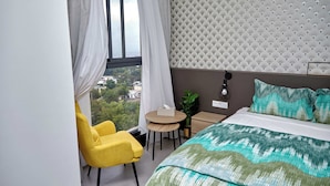 A modern hotel room with a bed, a yellow armchair, a small round table, and a view of the city through large windows. - Waypoint Suites (Dakar)