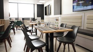 A modern dining area with booths and tables, a menu stand, and a TV mounted on the wall. - Waypoint Suites (Dakar)