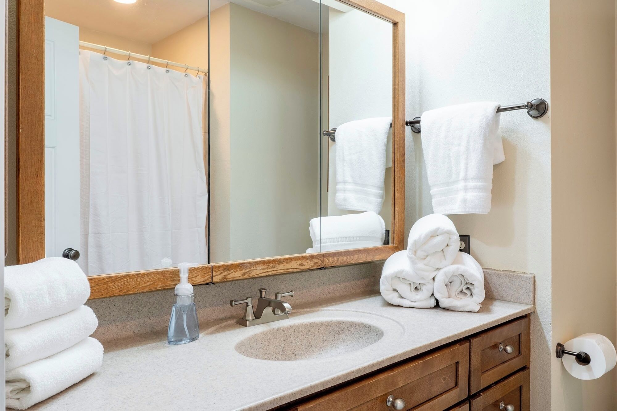A bathroom with a sink, mirror, towel rack, and a bottle of hand sanitizer.