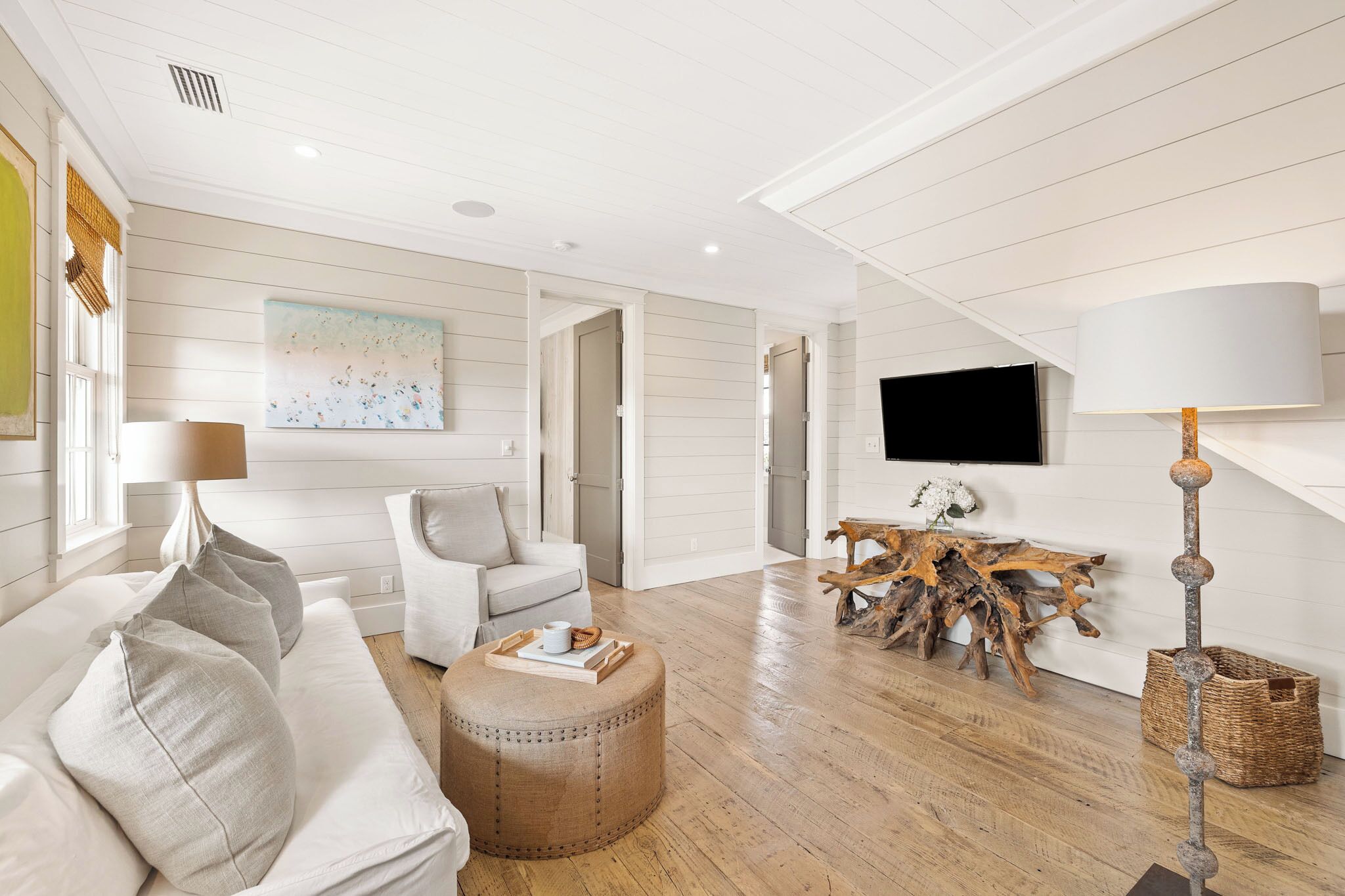 A modern living room with a white sofa, a round ottoman, a coffee table, a wooden side table, and a television mounted on the wall.