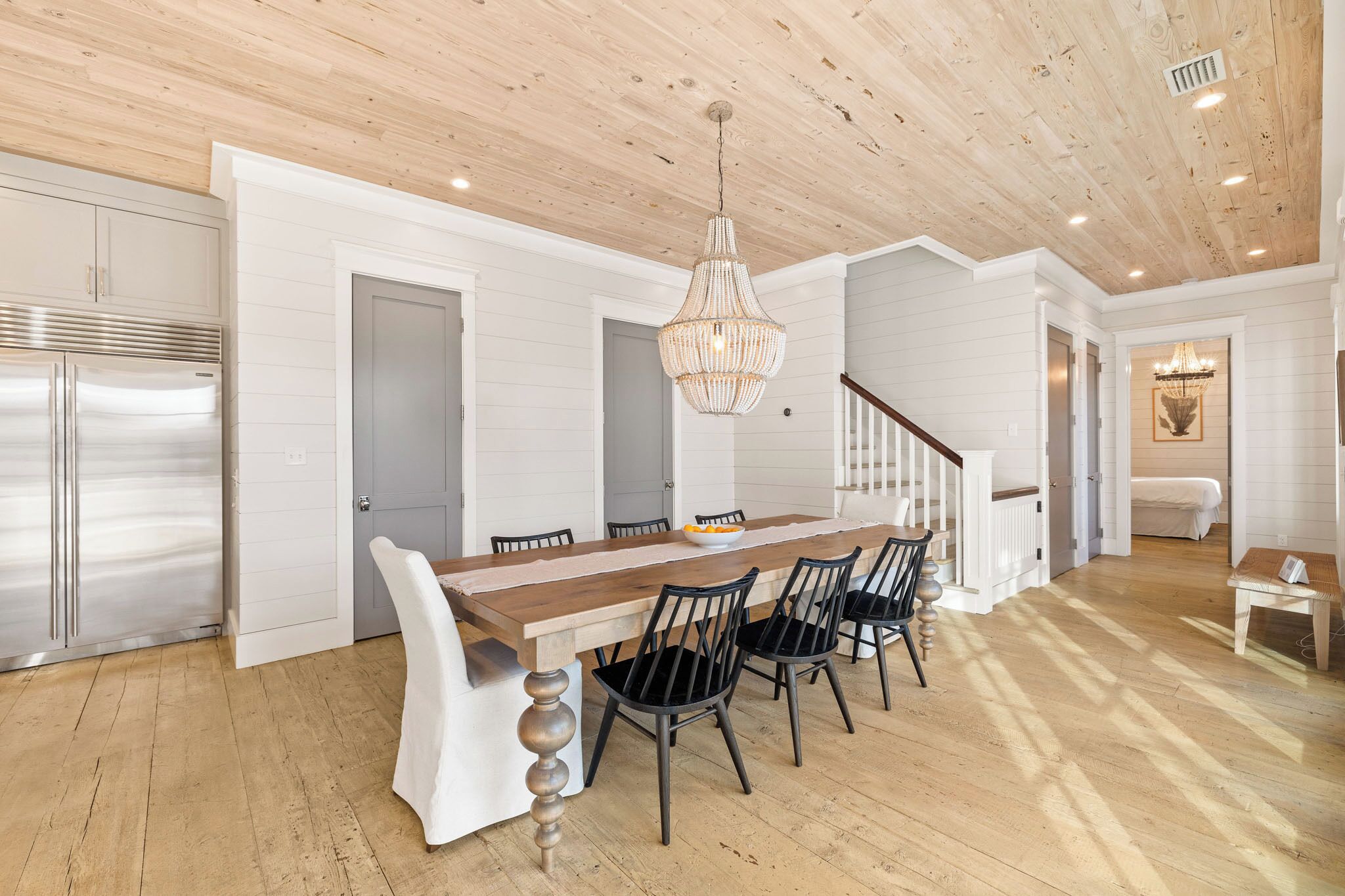 A modern kitchen with a wooden ceiling, white walls, and a large dining table with chairs.