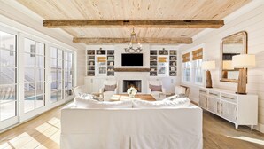 A spacious living room with a fireplace, white furniture, and large windows.