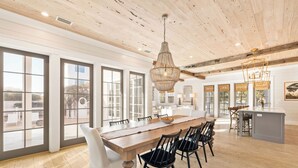 A spacious dining area with a wooden table and chairs, large windows, and a hanging light fixture.
