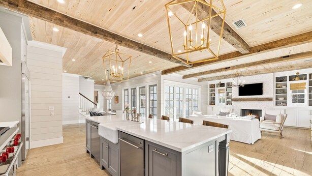A spacious kitchen with a large island, wooden ceiling beams, and modern pendant lighting.