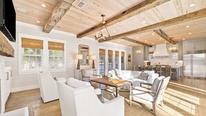 A spacious living room with white sofas, a wooden coffee table, and a large chandelier.