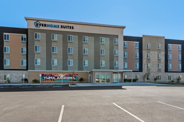 Un hotel moderno con varios pisos, un mural acogedor y un área de estacionamiento despejada.