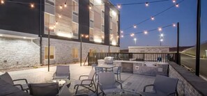 Une terrasse extérieure avec des sièges et un barbecue, entourée de murs en pierre et illuminée de guirlandes lumineuses.