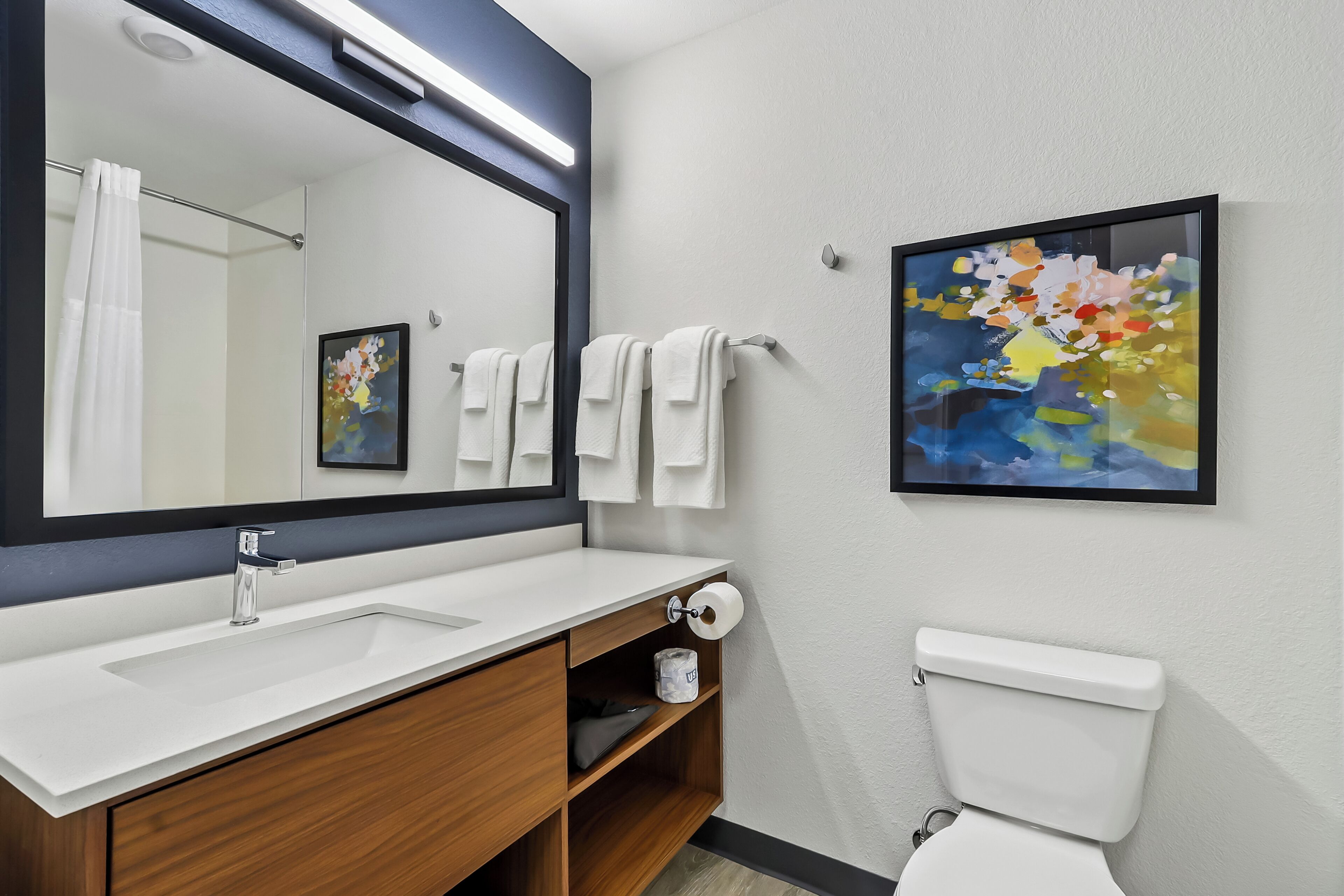 Un baño moderno con un espejo grande, lavamanos blanco y retrete.