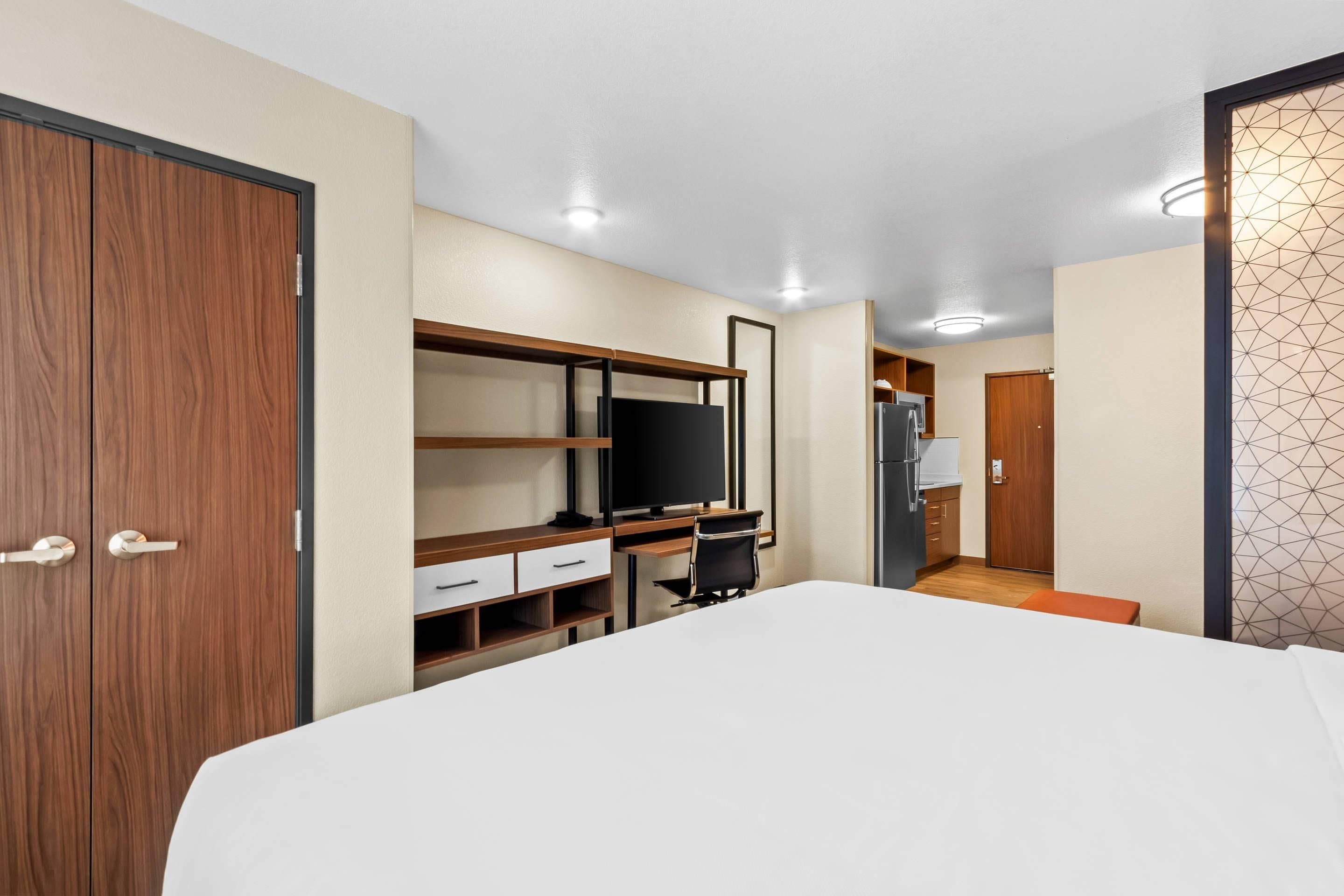 A hotel room with a bed, a desk with a computer, a TV, and a wardrobe.
